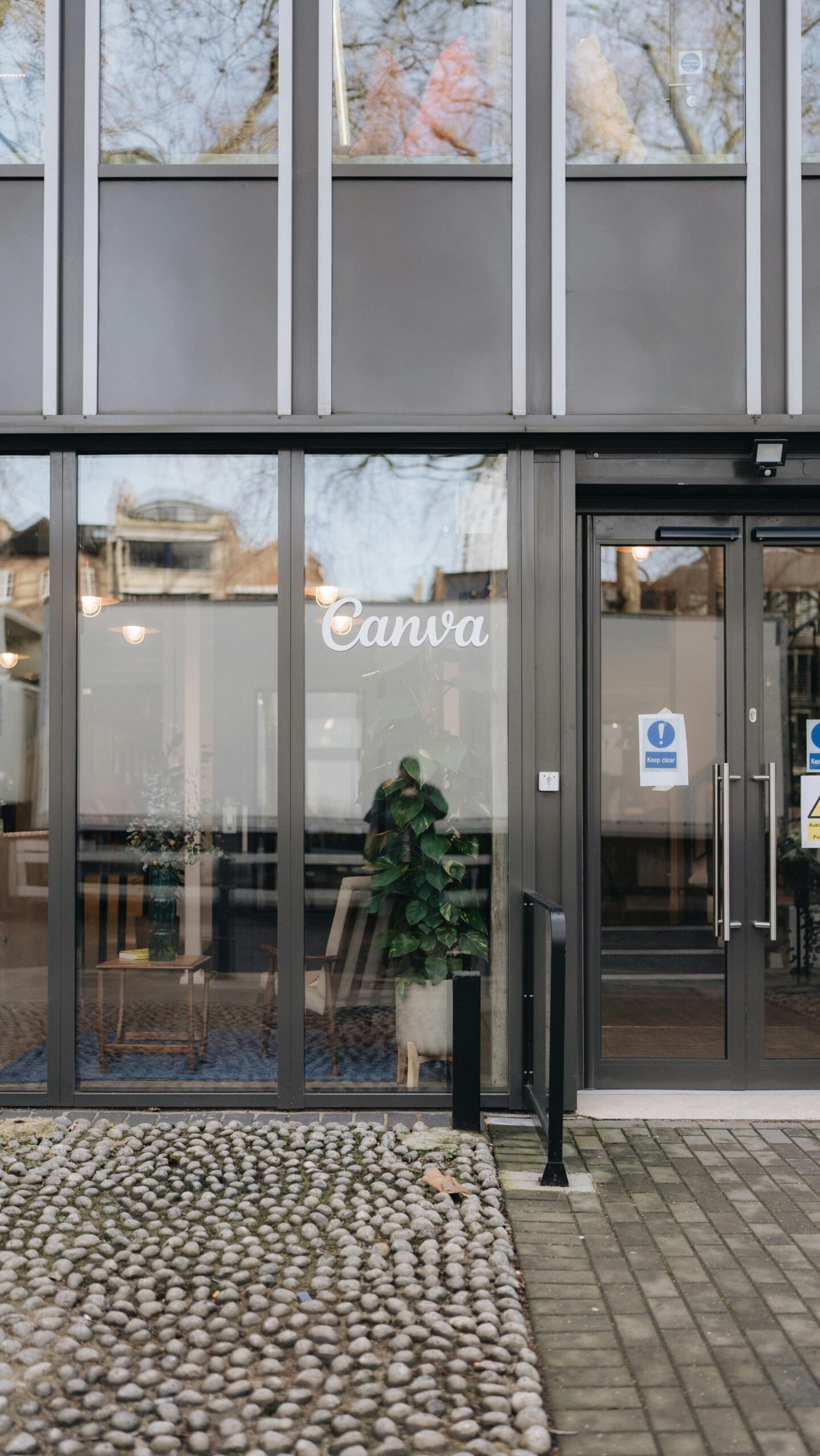 Entrance to a modern office building with large glass windows and a pebbled pathway.